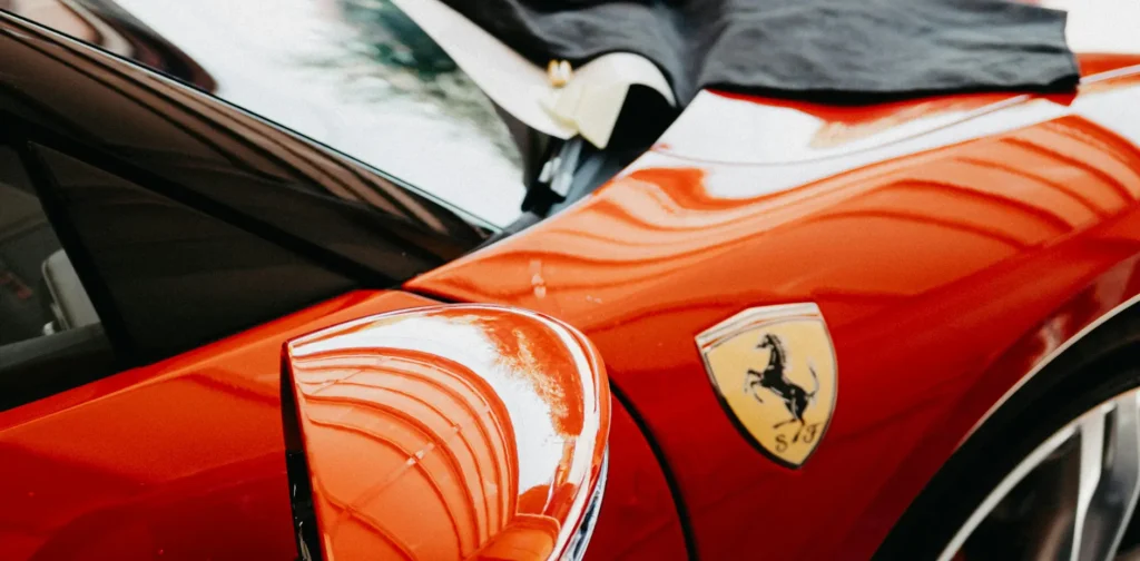 A red Ferrari sports car parked inside a spacious garage with concrete walls and bright overhead lighting