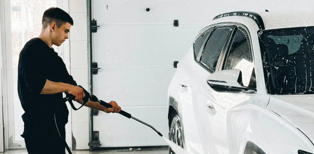 A man is washing a white car inside a garage, focusing on cleaning the vehicle's exterior
