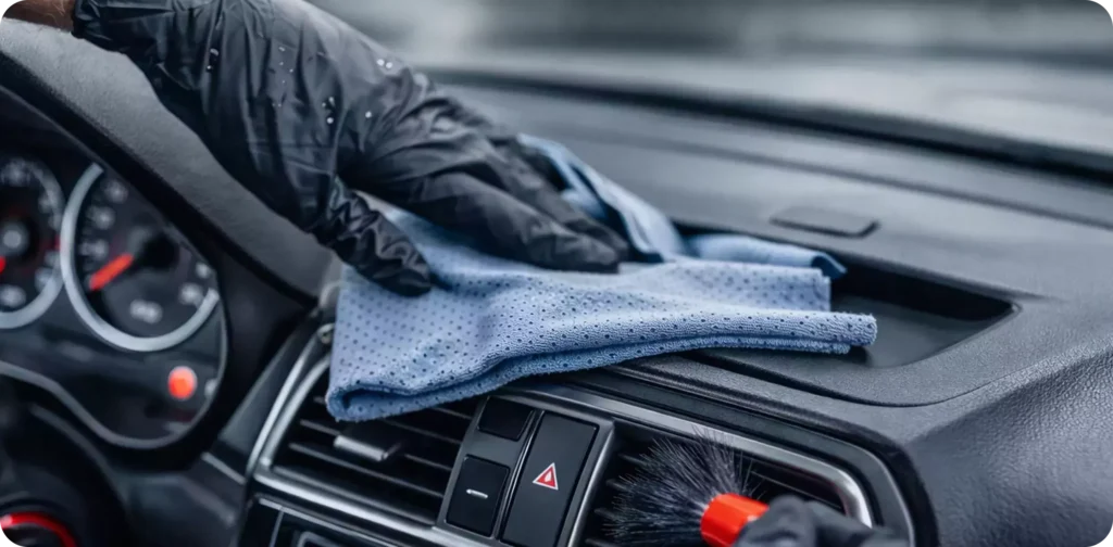A person using a cloth to clean the dashboard of a car, focusing on removing dust and dirt