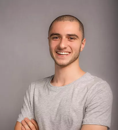 Portrait of a young man smiling, showcasing a friendly expression and bright eyes against a neutral background