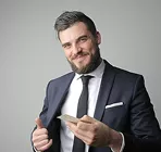 A man in a suit and tie holds a piece of paper, looking confidently at the camera