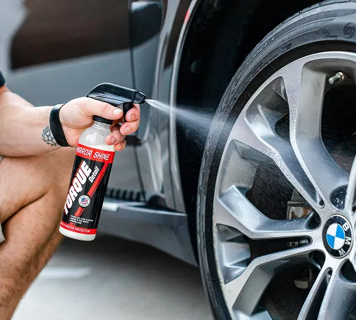 A man sprays tire cleaner onto a tire, focusing on cleaning its surface for better appearance and maintenance