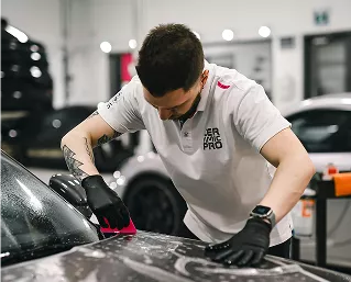 A man is using a rag to clean the exterior of a car, focusing on the surface for a polished finish.