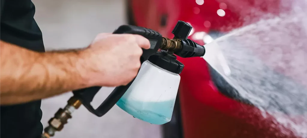 A person uses a sprayer to wash a car, spraying water and soap onto the vehicle's surface.